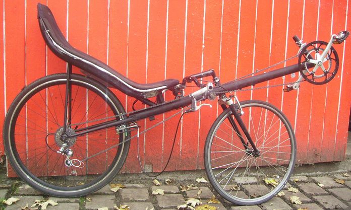 aeroproject l1 Ein recumbent Fahrrad mit langem Rahmen und bequemer Rückenlehne vor roter Wand.