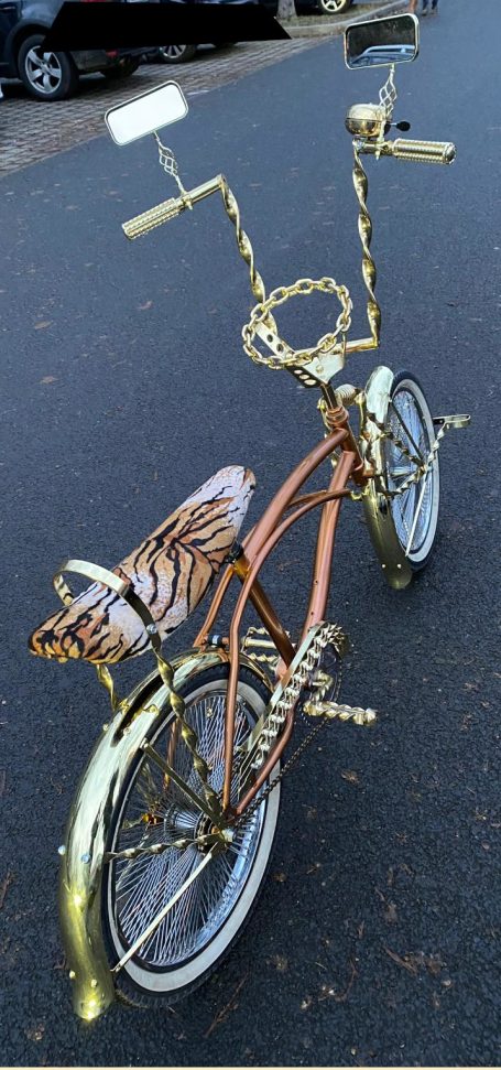 Ein goldfarbener Fahrradrahmen mit verzierten Griffen und einem einzigartigen Design.